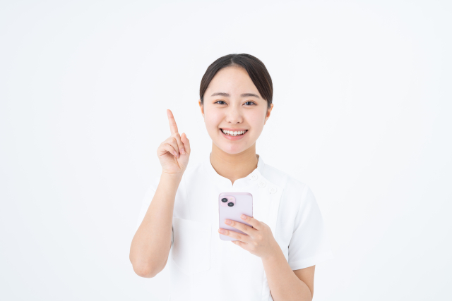 スマートフォンを持って笑顔で人差し指を立てるポーズの女性看護師