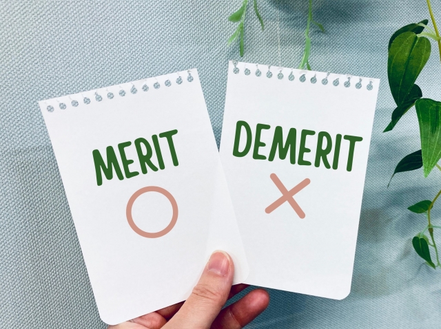 「MERIT〇」「DEMERIT×」と書かれた2枚のカードを掲げているイラスト