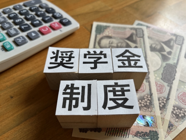 紙幣の上にブロックで「奨学金制度」と書かれたイラスト