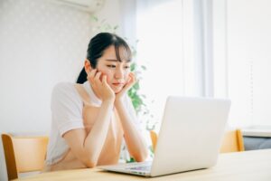 ノートPCを前に頬杖をついて悩んでいる女性の画像