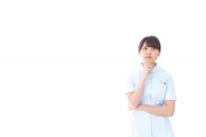 右手を顎にあてて考えるポーズの女性看護師の画像